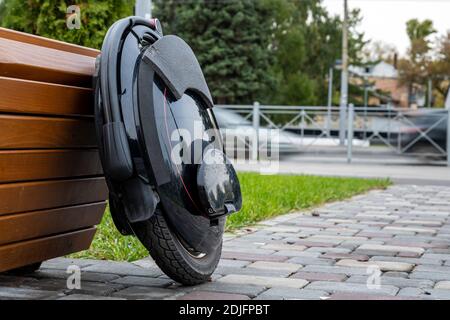 Schwarzes elektrisches Mono-Rad, innovatives persönliches Fahrzeug, selbstbalancierendes Elektro-Einrad, ökologischer urbaner Transport der Zukunft in der Nähe einer Holzbank Stockfoto