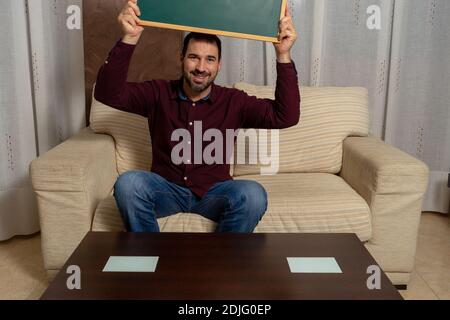 Bärtiger Mann, der zu Hause mit dem Daumen nach unten auf der Couch sitzt. Konzept der Hoffnungslosigkeit Stockfoto