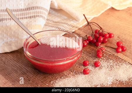 Rote Beeren des Viburnums, gemahlen mit dem Zucker in der Glasvase auf dem hölzernen Tisch. Vitaminsüße. Stockfoto