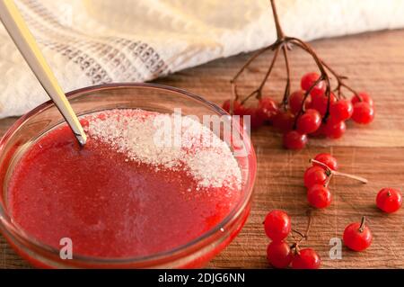 Rote Beeren des Viburnums, gemahlen mit dem Zucker in der Glasvase auf dem hölzernen Tisch. Vitaminsüße. Stockfoto