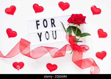 Valentinstag, Liebe, romantisches Konzept. Frische rote Rose Blume mit Band und Text für Sie auf Leuchtkasten auf weißem Hintergrund. Grußkarte. Flache Lay, Stockfoto