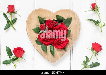 Valentinstag, Liebe, romantisches Konzept. Rote Rosen und Herz aus Holz auf weißem Hintergrund. Flach liegend, Draufsicht. Stockfoto