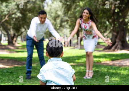 Portrait von glücklichen schönen Familie von drei zu Fuß im Park. Mama, Papa und kleiner Sohn genießen Freizeit im Sommer. Verwirrt kleiner Sohn Stockfoto