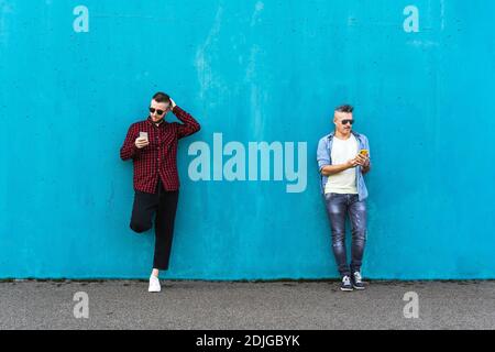 Coole Männer suchen Handy lehnen sich gegen blaue Wand im Freien - paar Freunde süchtig nach Technologie und sozialen Netzwerken - Konzept der Tech, SoC Stockfoto