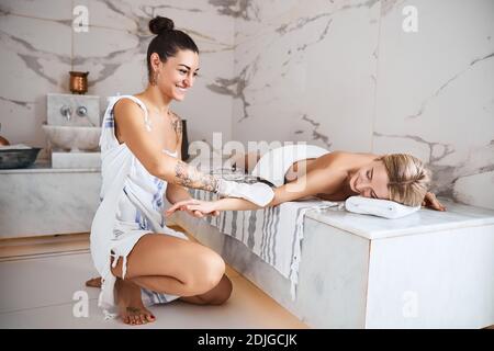 Elegante sorgfältige Frau in Peschtemal Handtuch macht Massage auf die Frau Hand in Beauty-Center Stockfoto