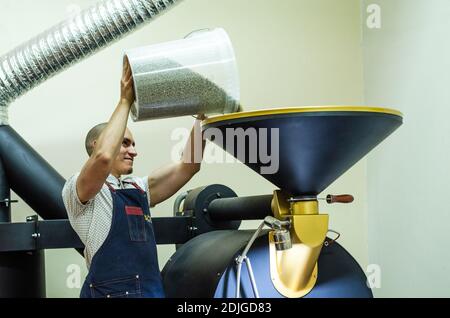 Mann gießt rohe Kaffeebohnen in eine Kaffeeröstermaschine Stockfoto