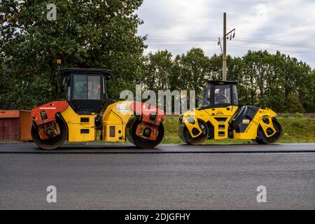KIEW, UKRAINE - 25. September 2020: Schwere gelbe Asphaltwalze mit schweren Vibrationswalzenverdichter, die neuen heißen Asphalt auf der Straße drücken Stockfoto