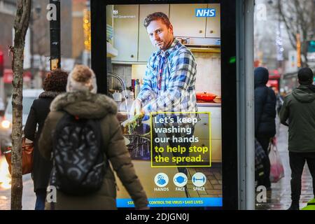 London, Großbritannien. Dezember 2020. Eine Frau schaut auf ein digitales Plakat der NHS COIVD-19-Kampagne in London. London wird am Mittwoch nach einer Erhöhung der COVID-19-Ansteckungsraten in die dritte Kategorie wechseln. Kredit: SOPA Images Limited/Alamy Live Nachrichten Stockfoto