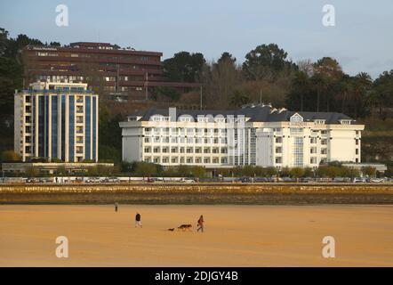 Menschen Hund zu Fuß am Strand an einem frischen windigen Spätherbst Morgen Sardinero Santander Cantabria Spanien Hotel Chiqui Apartmentgebäude Stockfoto