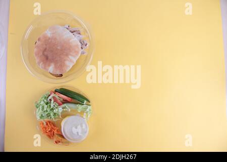 Ein Gyro-Sandwich in einer Kunststoffschale - Brot und Zutaten für die Herstellung Gyro isoliert auf gelbem Hintergrund flach legen. Das Bild enthält den Kopierbereich Stockfoto