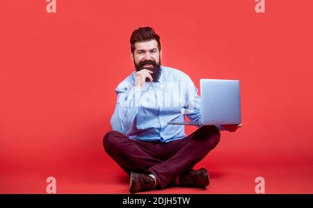 Halten Laptop-Computer.Junge Geschäftsmann mit seinem Laptop, pc. Lächelnd schöner bärtiger Mann Arbeiter Laptop. Glücklicher junger Mann, der mit auf dem Boden sitzt Stockfoto