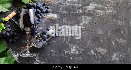 Weingläser mit Rotwein und Trauben. Trauben mit Blättern und Reben Korken auf dunklen rustikalen Beton Hintergrund. Flach legen Weinzusammensetzung auf Stockfoto