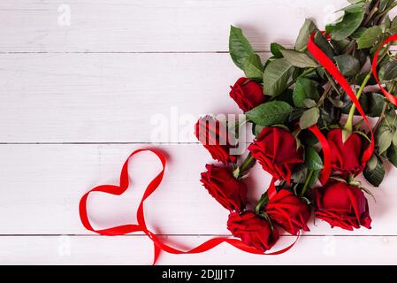 St. Valentines Day Konzept. Rotes Band in Herzform, Strauß von Rosen und Geschenkschachteln in Kraftpapier Papper auf weißem Holztisch eingewickelt. Stockfoto