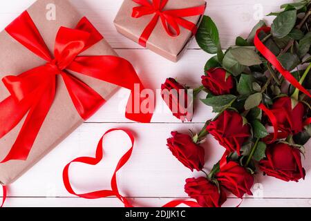 St. Valentines Day Konzept. Rotes Band in Herzform, Strauß von Rosen und Geschenkschachteln in Kraftpapier Papper auf weißem Holztisch eingewickelt. Stockfoto
