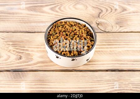 Tierfutter in einer Schüssel auf einem hölzernen Vintage-Hintergrund. Trockenfutter für Hunde oder Katzen in einer Schüssel auf Holzgrund. Stockfoto