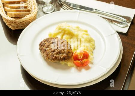 Gebratene Koteletts mit Kartoffelpüree und reifen frischen Tomaten auf dem weißen Gericht, mit Weißbrot, serviert im Restaurant. Stockfoto