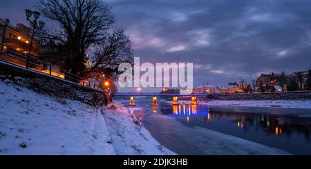 uzhhorod, ukraine - 26 DEC 2016: Winterliche Stadtlandschaft bei Sonnenaufgang. Wunderschöne Landschaft an der uzh. Lichter der Stadt spiegeln sich im Wasser. Schnee am Ufer Stockfoto