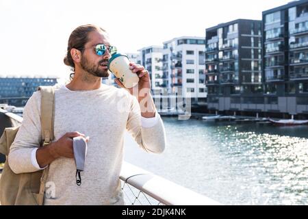 Junger Mann mit Kaffeetasse und Gesichtsmaske aus und Über in der Stadt Stockfoto