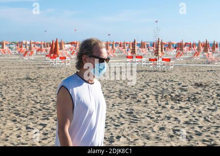 Man walking on a desert beach in Italy and wearing a Covid-19 protective face mask Stock Photo