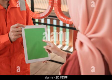 Nahaufnahme eines Mechanikers im Wearpack mit einem digitalen Tablet mit einem Kunden im Hintergrund eines Reifens Rack Stockfoto