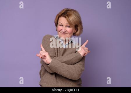 Reife Frau gefüllt mit Zögern und Zweifeln, Punkte mit Zeigefinger in verschiedenen Seiten, zeigt zwei Wege auf links und rechts, hat rätselhafte Ausdruck Stockfoto