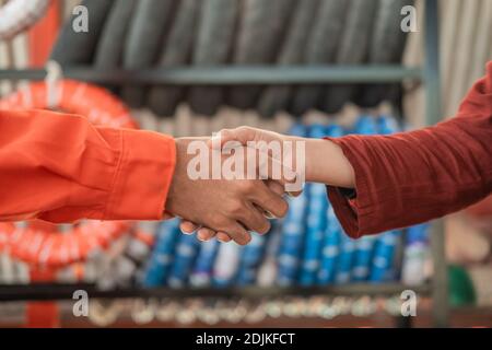 Hände des männlichen Mechanikers in einer Wearpack Uniform schütteln die Hände Mit einer Kundin im Hintergrund eines Reifens Rack Stockfoto