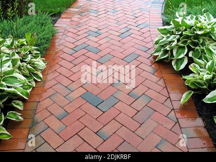 Backsteinweg schlängelt sich durch einen schönen Garten. Stockfoto