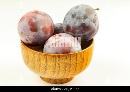 Einige reife lila Pflaumen in einer Holzschale auf weißem Hintergrund. Stockfoto