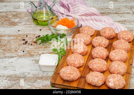 Frische Fleischbällchen mit Gewürzen und Olivenöl auf dem natürlichen Holztisch zum Kochen vorbereitet. Stockfoto