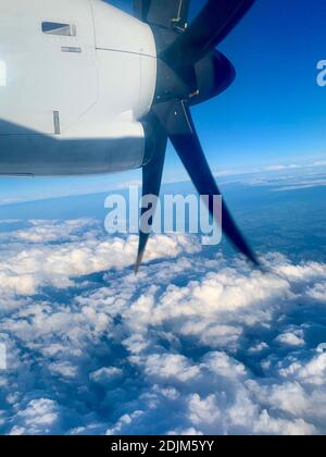 Blick von einem Flugzeugfenster auf den blauen Himmel, die Wolken unten und den Propeller einer Turboprop-Maschine Stockfoto