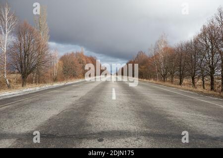 Leere Winterstraße ohne Schnee, mit Bäumen ohne Blätter an den Seiten Stockfoto