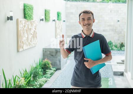 Männlicher Gehäuseentwickler steht beim Tragen mit Daumen nach oben Das Zertifikat des Hauses auf der Homepage Stockfoto