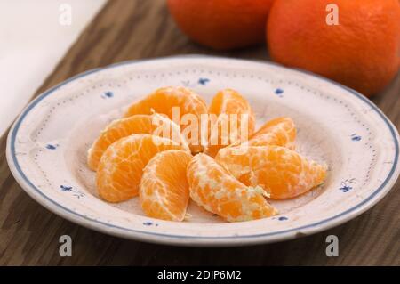Nahaufnahme einer Platte mit den Scheiben einer Mandarine Neben einigen ungeschälten Mandarinen Stockfoto