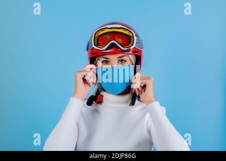 Nahaufnahme Porträt eines Mädchen Skifahrer trägt eine leichte blu Schutzmaske, Helm und Brille. Ein Snowboarder auf hellem blu-Hintergrund. Covid19 Coronavir Stockfoto