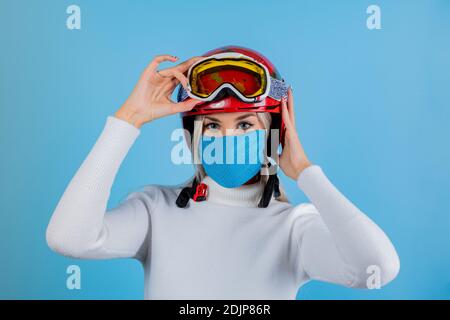 Nahaufnahme Porträt eines Mädchen Skifahrer trägt eine leichte blu Schutzmaske, Helm und Brille. Ein Snowboarder auf hellem blu-Hintergrund. Covid19 Coronavir Stockfoto
