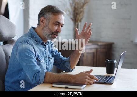 Porträt von grauhaarigen Senior gutaussehend lächelnden Mann von zu Hause aus arbeiten. Kommunikation online mit Kollegen und Videokonferenz. Online-Meeting Stockfoto
