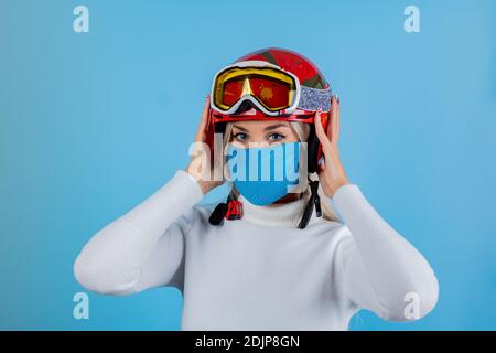 Nahaufnahme Porträt eines Mädchen Skifahrer trägt eine leichte blu Schutzmaske, Helm und Brille. Ein Snowboarder auf hellem blu-Hintergrund. Covid19 Coronavir Stockfoto
