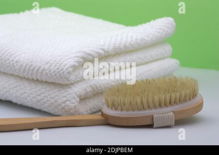 Folded white towels next to a natural bristle shower brush on a green background and a white table Stockfoto