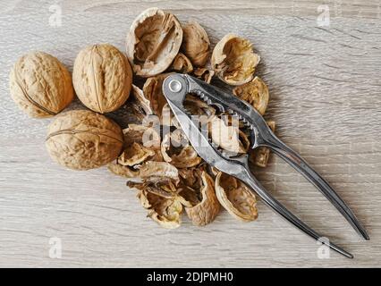 Three whole walnuts, nutshell and nutcracker on a wooden table Stock Photo