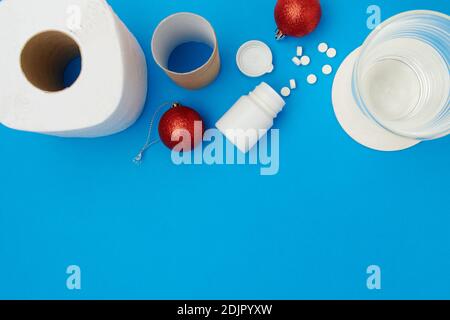 Flaches Lay mit weihnachtskugel, Toilettenpapier, Pillen und Glas Wasser auf blauem Hintergrund. Stockfoto