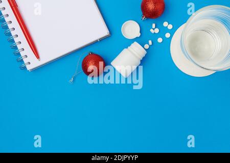 Flach legen mit weihnachtskugel, Pillen und Glas Wasser auf blauem Hintergrund. Stockfoto