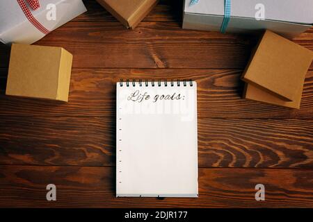 Wooden table with gift boxes and notepad with list of life goals. Space for writing purposes. Boxes are tied with colored ribbons. Concept of Christmas new year. Open spiral notebook. Stockfoto