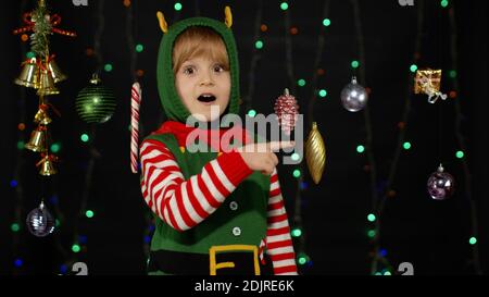 Teen Kind Mädchen in Weihnachten elf Santa Claus Helfer Kostüm zeigt auf etwas und zeigt Daumen nach oben Geste, zustimmen Zeichen isoliert auf schwarzem Hintergrund. Lächelndes Kind. Neujahrsfeierlichkeiten Stockfoto
