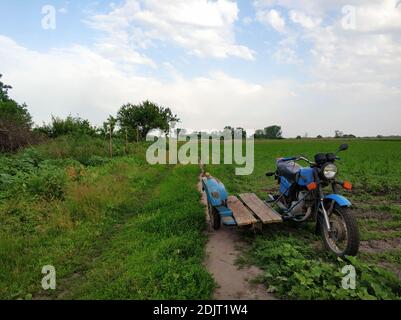 Altes Motorrad mit Seitenwagen auf einer verlassenen Dorfstraße im Feld. Verkehr auf dem Land. Stockfoto