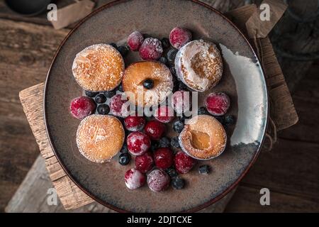 Verschiedene gefrorene Beeren und Früchte in einem braunen Teller auf einem hölzernen Hintergrund. Stockfoto