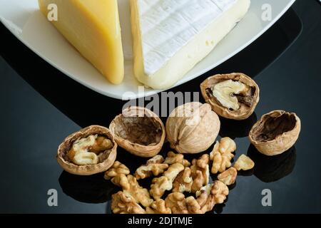 Walnüsse auf glänzendem schwarzem Hintergrund neben Parmesan und Brie-Käse. Stockfoto