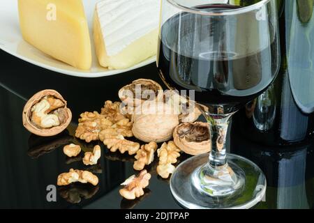 Nüsse neben Parmesan und Brie. Ein Glas Rotwein im Vordergrund. Stockfoto