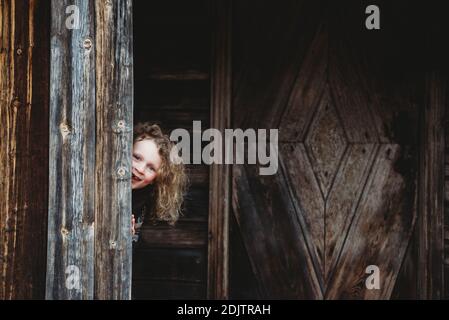 Liebenswert blonde Mädchen spielen verstecken und suchen versteckt in alt Holzhaus Stockfoto