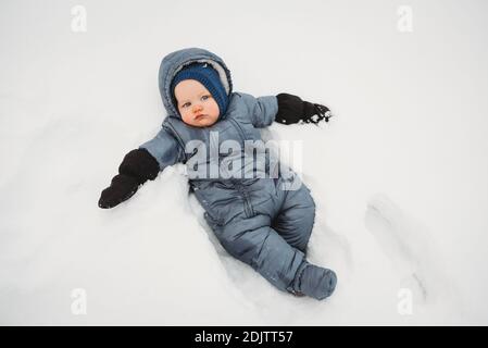 Adorable Baby suchen traurig liegend auf Schnee trägt einen snowsui t Stockfoto