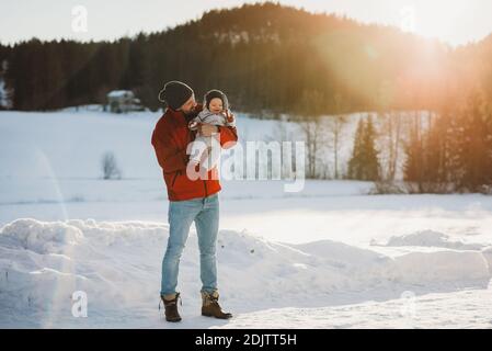 Papa und niedliches Baby im Wald voller Schnee Im Winter bei Sonnenuntergang Stockfoto